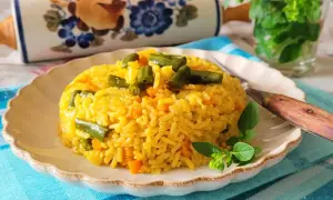 Ryż z curry, marchewką i fasolką szparagową na talerzu, ozdobiony ziołami.