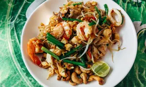 Talerz Pad Thai z krewetkami, kalmarami, kiełkami fasoli, orzechami nerkowca i limonką.