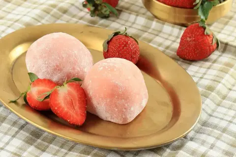 Różowe mochi z truskawkami na złotym talerzu.