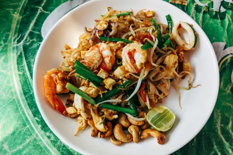 Talerz Pad Thai z krewetkami, kalmarami, kiełkami fasoli, orzechami nerkowca i limonką.