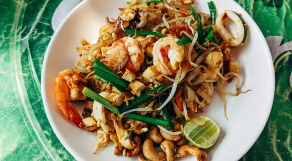 Talerz Pad Thai z krewetkami, kalmarami, kiełkami fasoli, orzechami nerkowca i limonką.