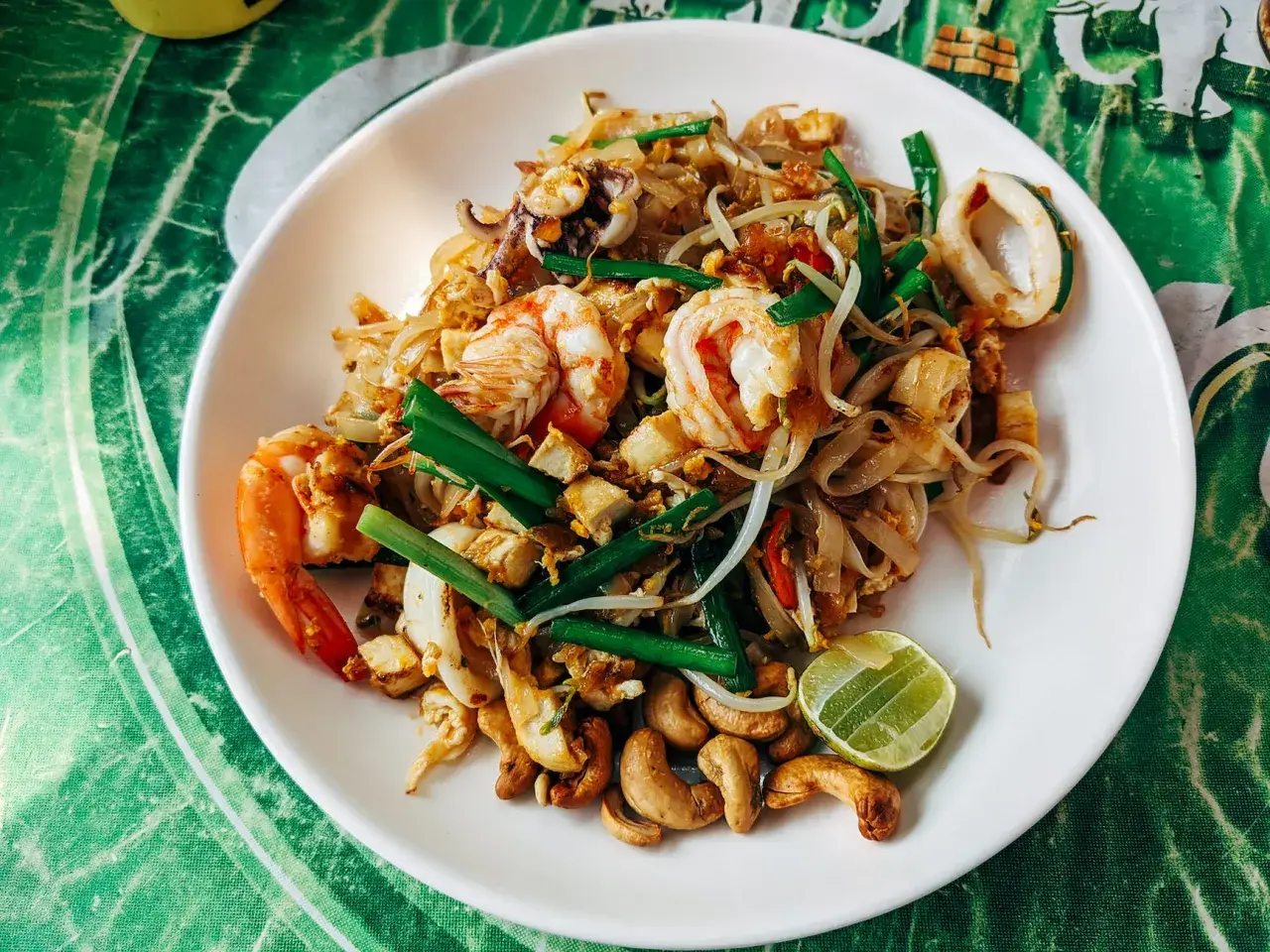 Talerz Pad Thai z krewetkami, kalmarami, kiełkami fasoli, orzechami nerkowca i limonką.