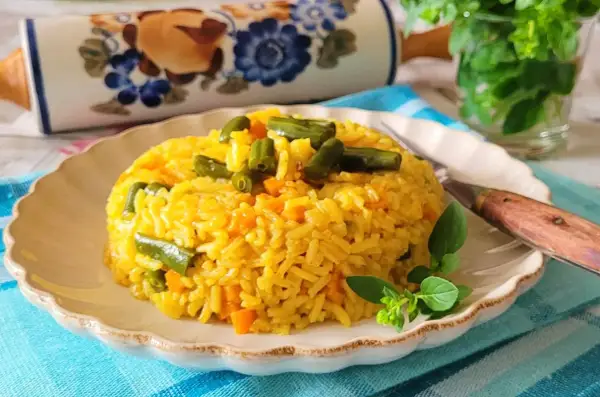 Ryż z curry, marchewką i fasolką szparagową na talerzu, ozdobiony ziołami.